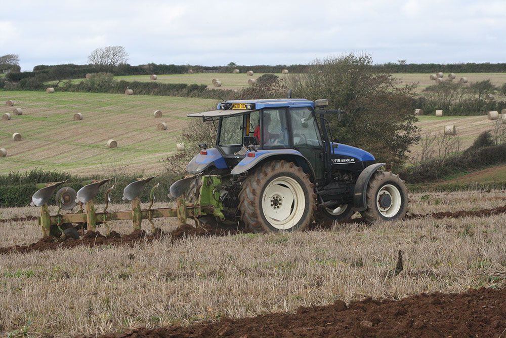 A blue tractor is plowing a field with a plow.