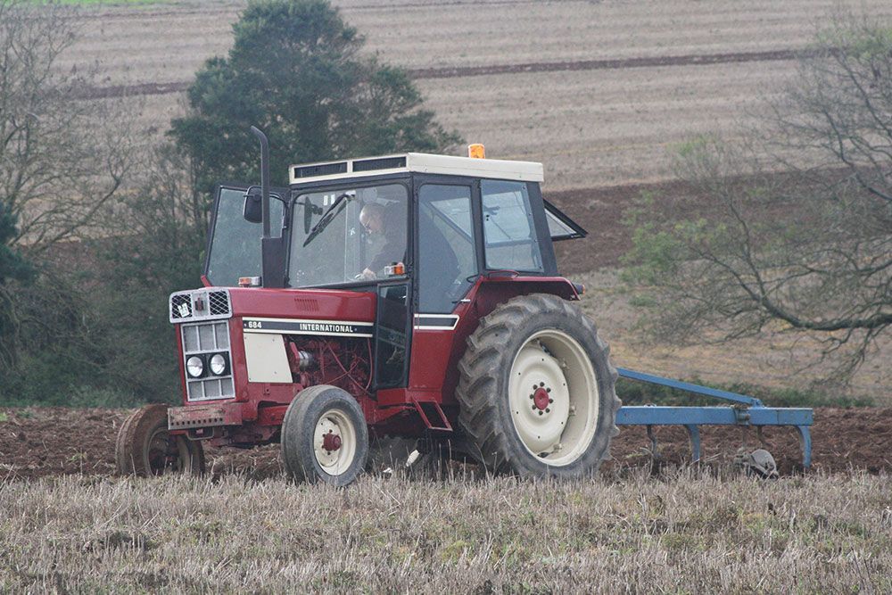 A red tractor is plowing a field with a plow attached to it.