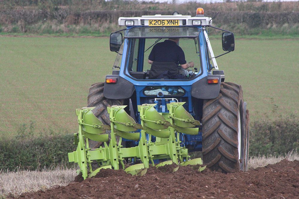 A man is driving a blue tractor in a field