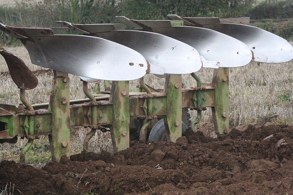 A green and silver plow is plowing a field