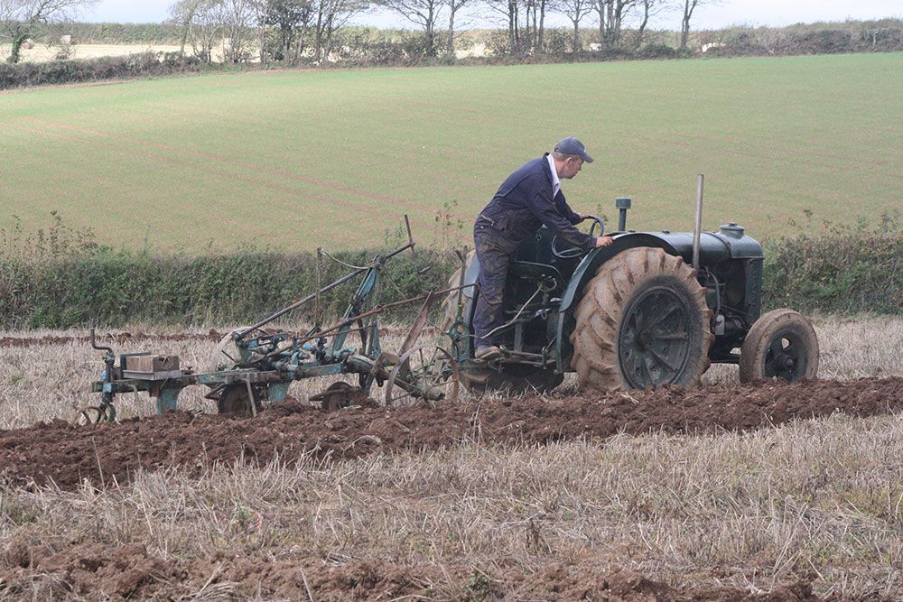 A man is plowing a field with an old tractor.