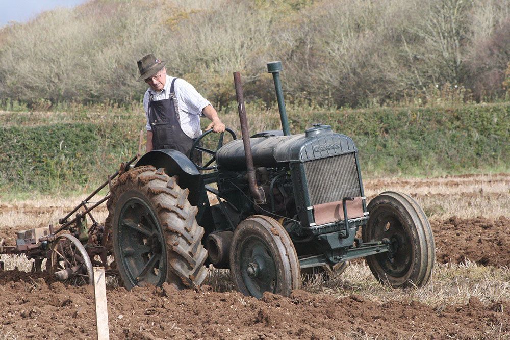 A man is plowing a field with an old tractor.