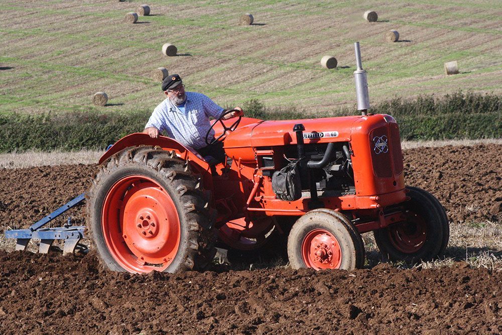 A man is plowing a field with an orange tractor