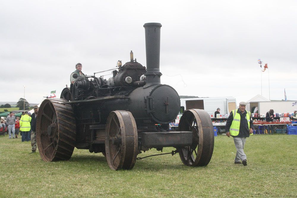 A man is standing next to an old steam engine in a field.