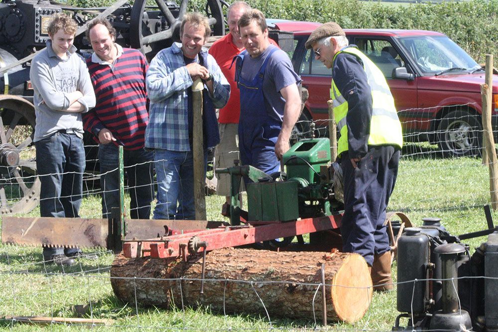 A group of men are looking at a machine that is cutting a log