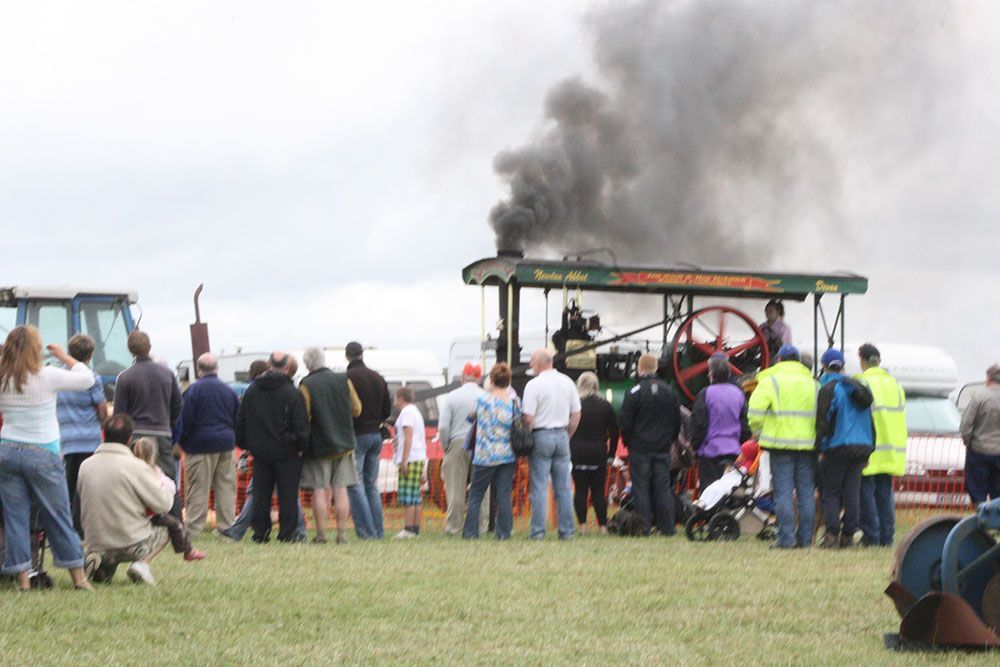 A group of people watching a steam engine with smoke coming out of it