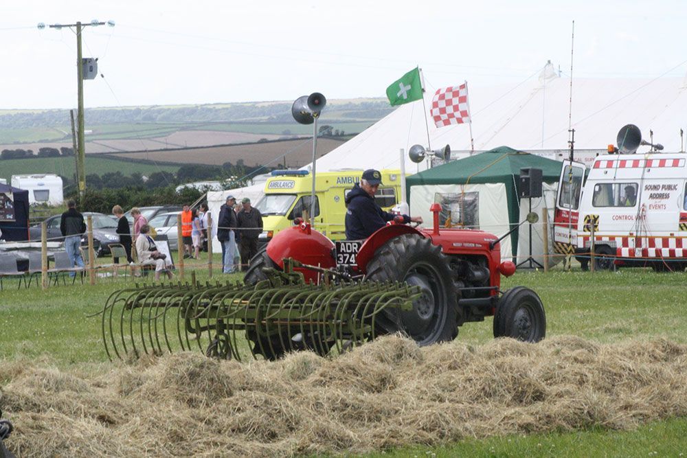A man is driving a red tractor with a rake attached to it.