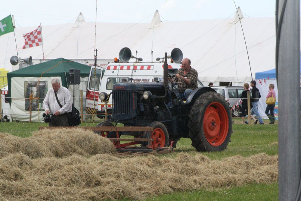 A man is driving a tractor in a field of hay.