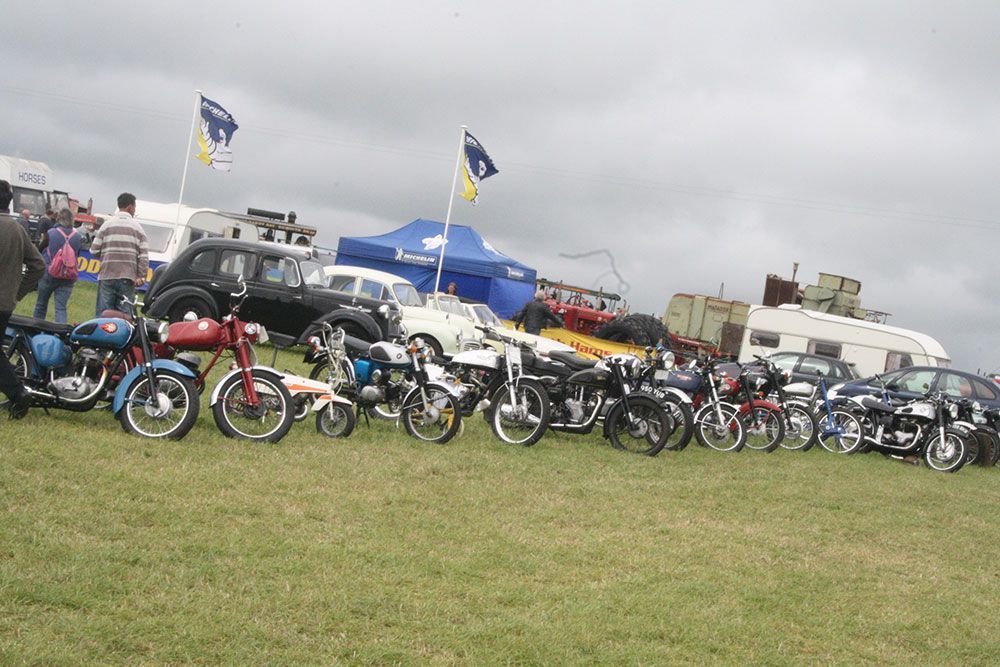 A row of motorcycles are parked in a grassy field