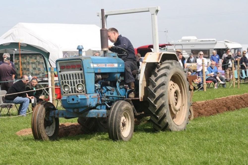 A man is driving a blue ford tractor in a field