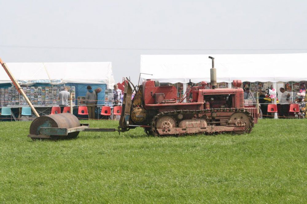 A red bulldozer is parked in a grassy field with a roller attached to it.