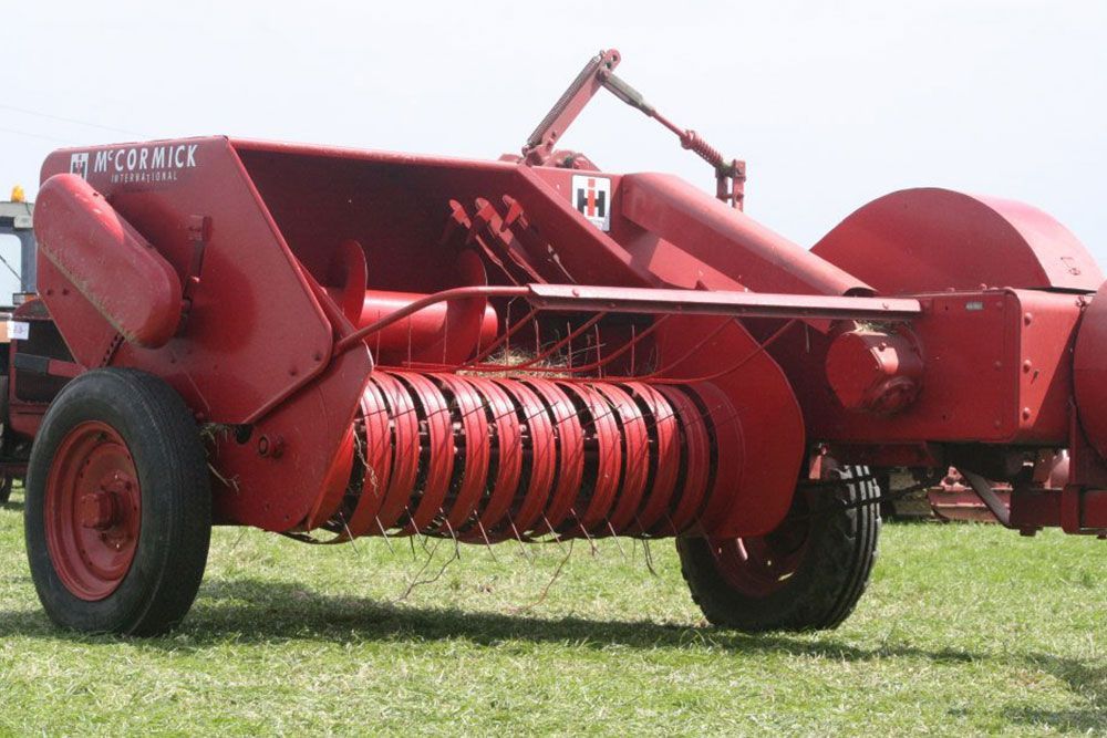 A red mccormick hay baler is parked in a grassy field