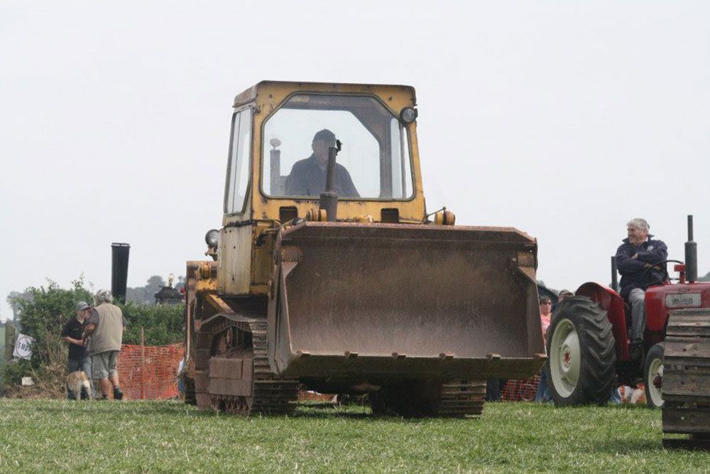 A yellow bulldozer is parked in a grassy field next to a red tractor.