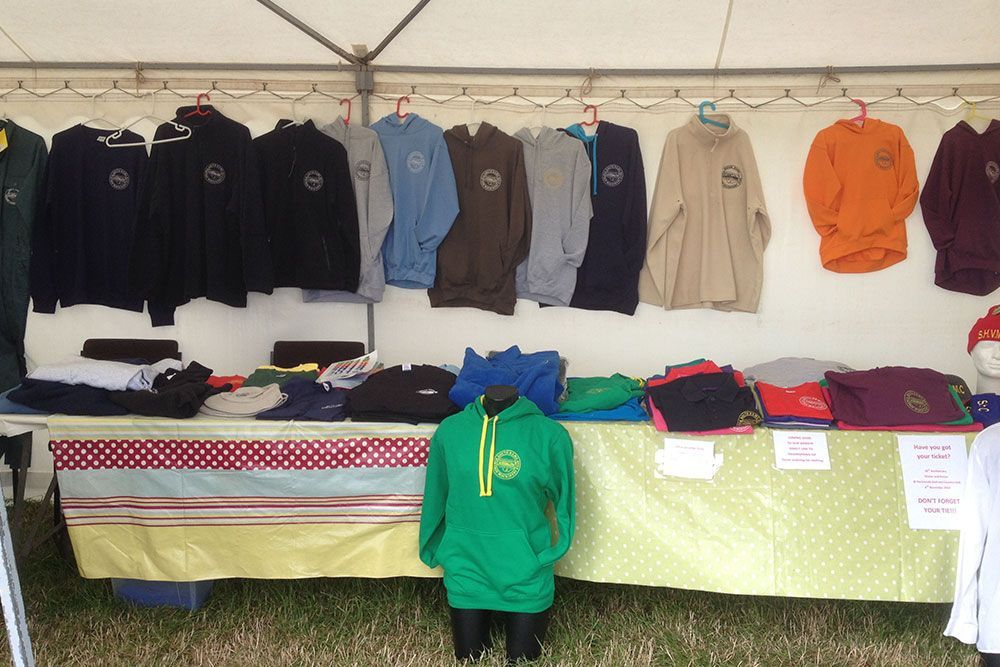 A green hoodie is on a mannequin in front of a table full of shirts