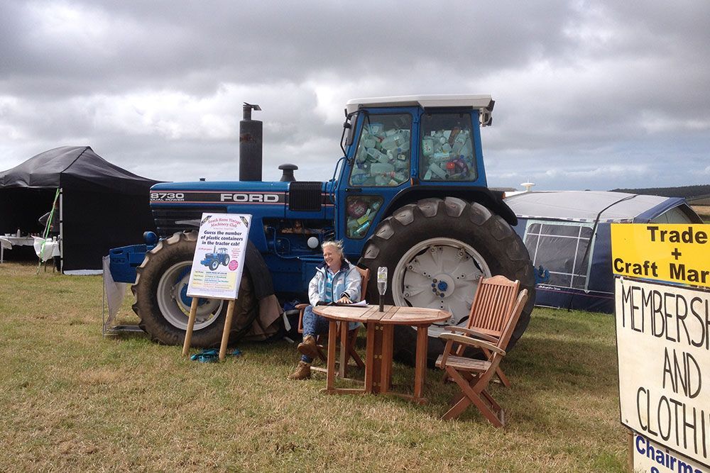A woman sits at a table in front of a blue tractor