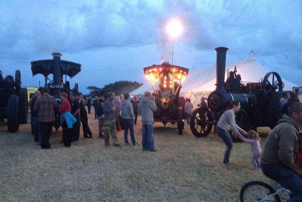 A group of people are standing in a field with a steam engine in the background