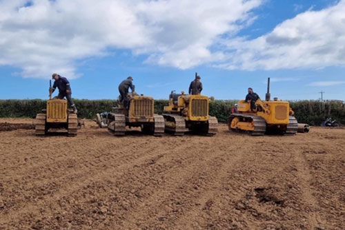 Three bulldozers are parked in a dirt field.