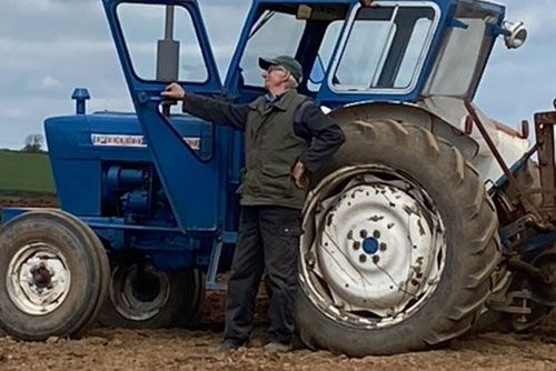 A man is standing next to a blue tractor in a field.