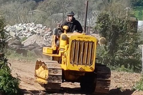 A man is driving a yellow bulldozer on a dirt road.