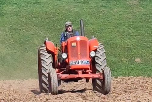 A man is driving a red tractor on a dirt road.