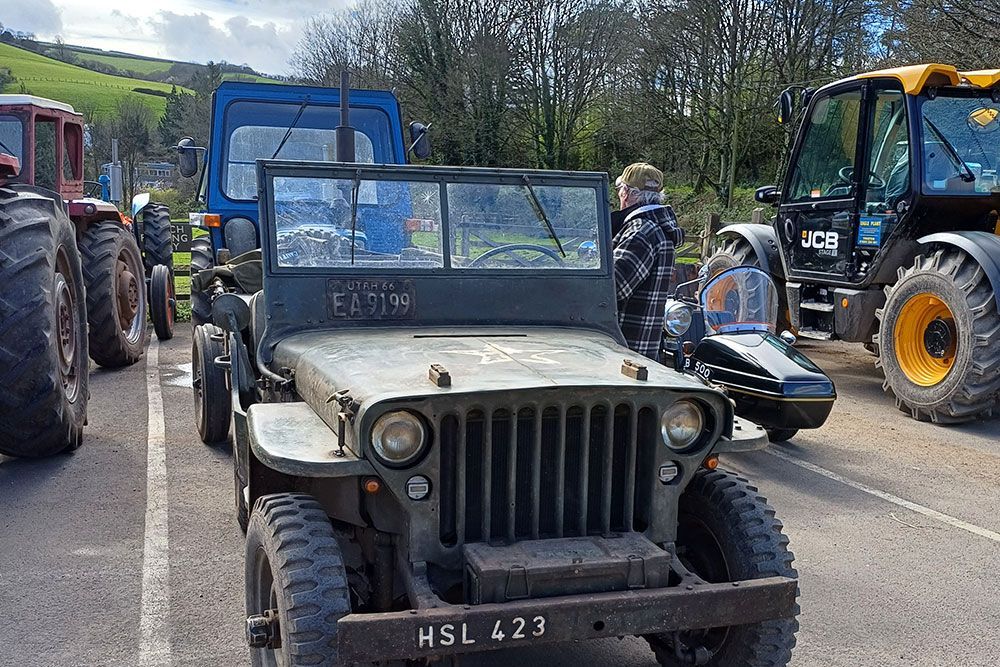 A jeep is parked on the side of the road next to a tractor.
