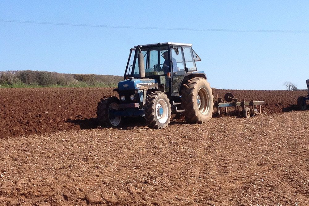 A blue tractor is plowing a dirt field
