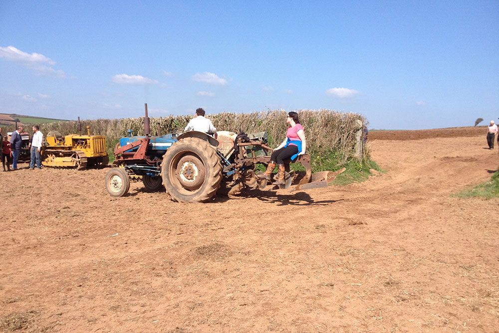 A group of people are sitting on a tractor in a dirt field.