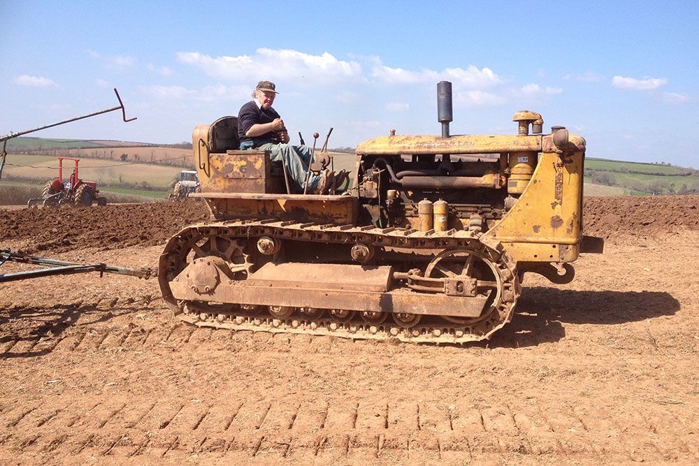 A man is sitting on a bulldozer in a dirt field