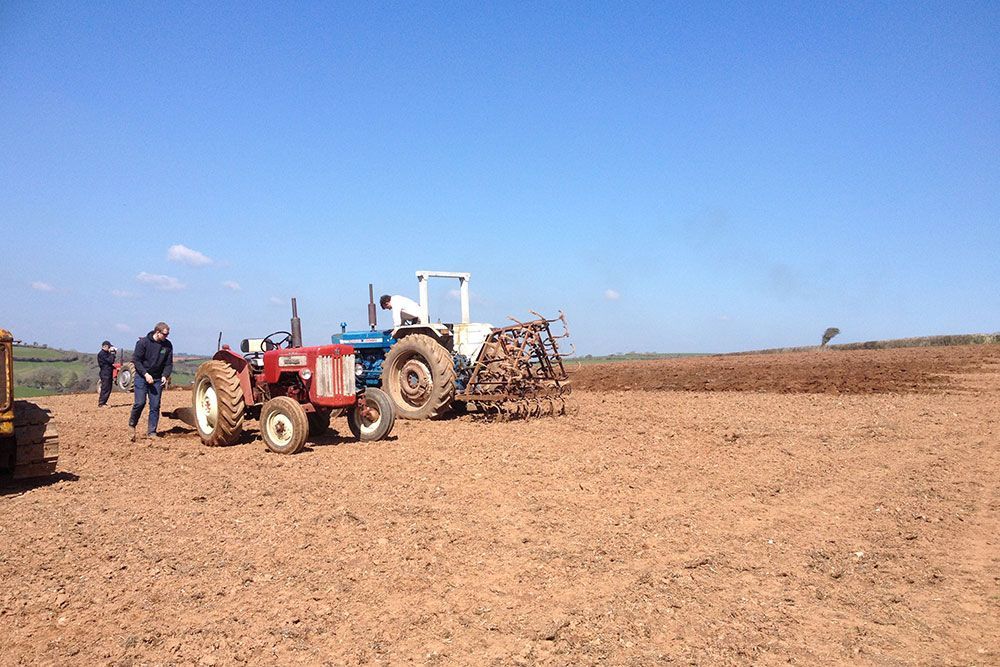 A group of tractors are plowing a field.