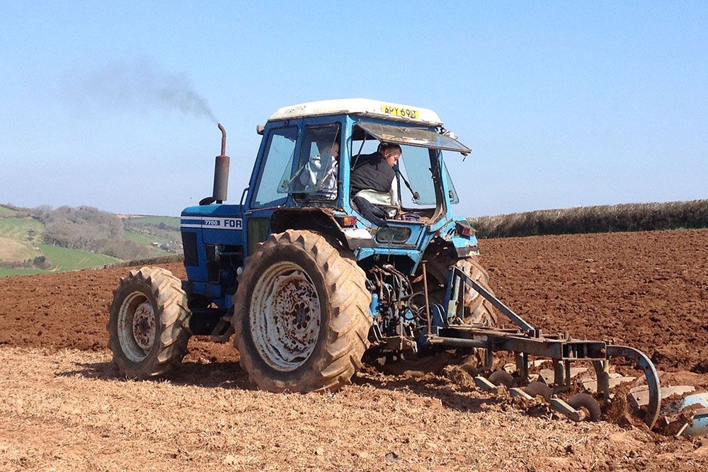 A man is driving a blue tractor in a field