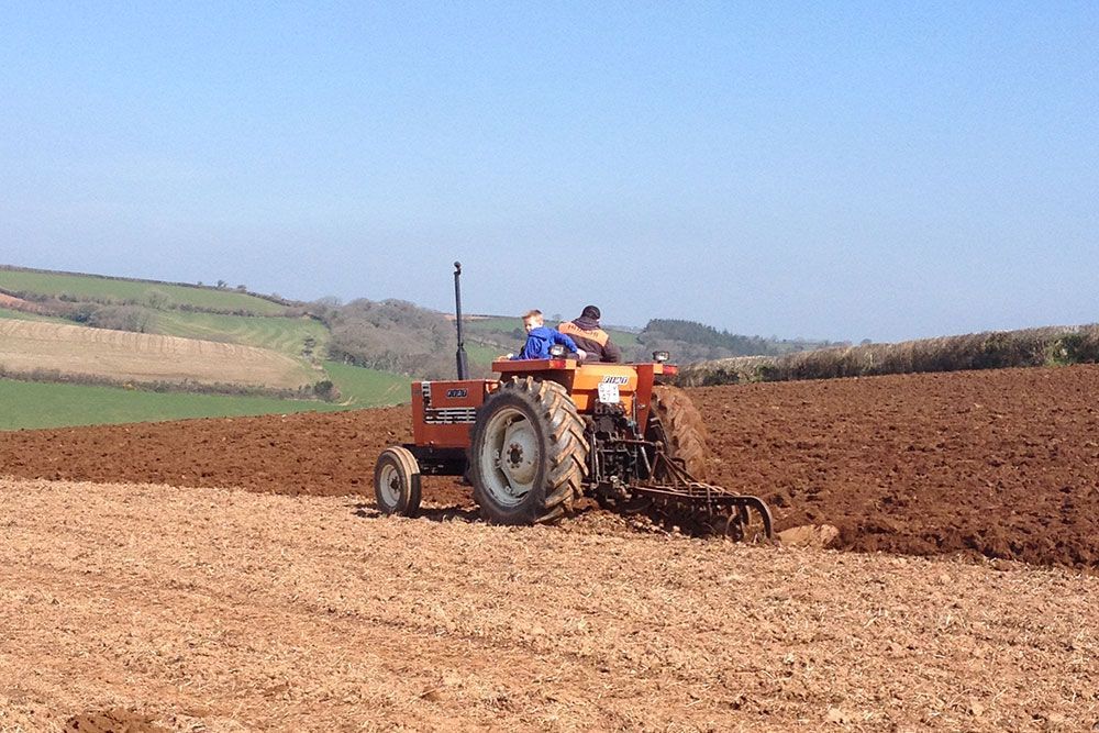 A man is driving a tractor through a dirt field.