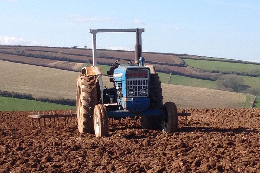 A blue ford tractor is plowing a field