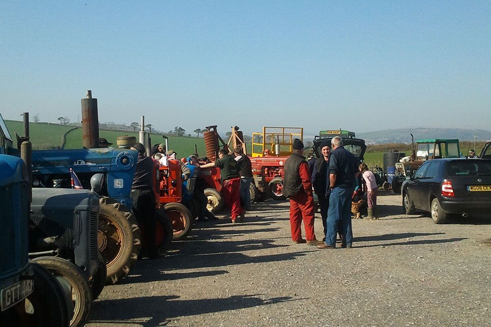 A group of people are standing in front of a row of tractors