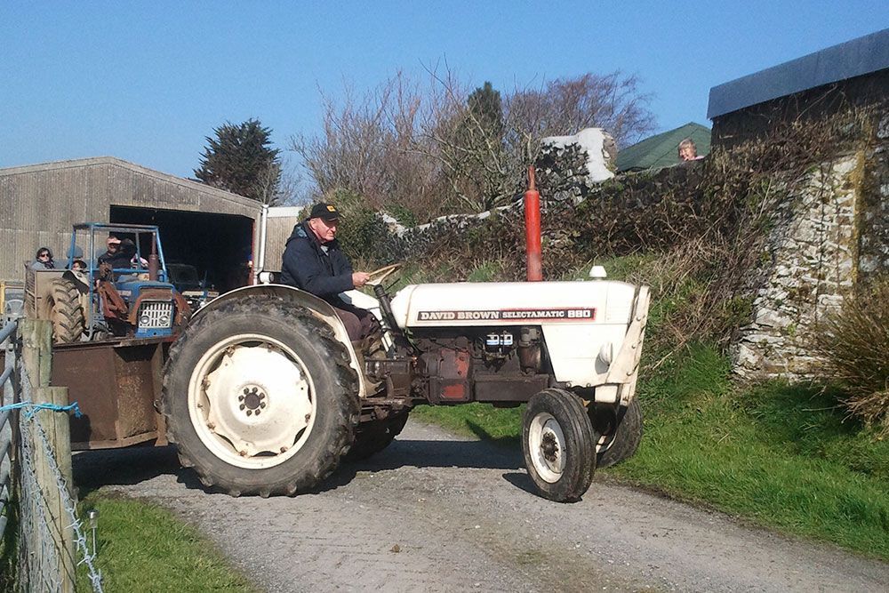 A man is driving a white tractor down a dirt road