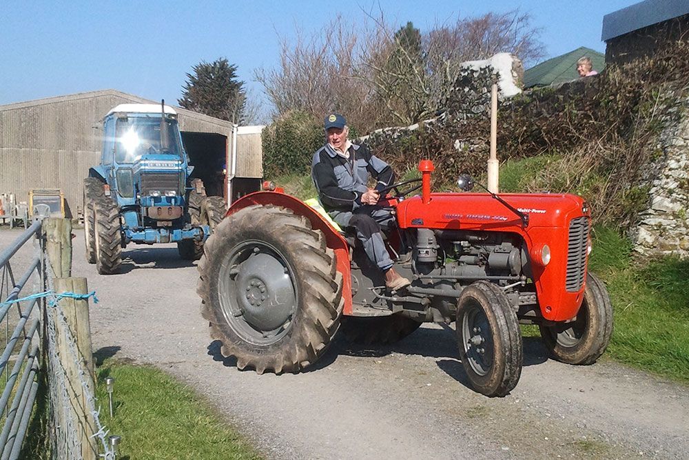 A man is driving a red tractor next to a blue tractor