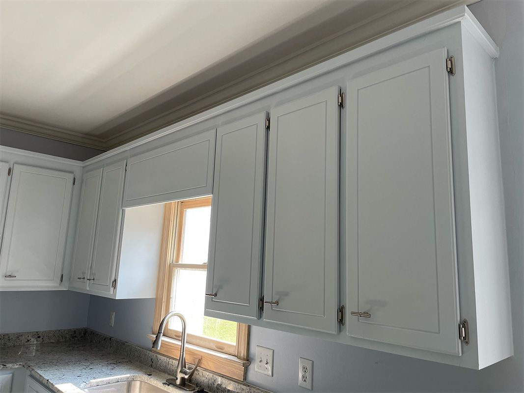 Light blue kitchen cabinets with hardware, near a window. 