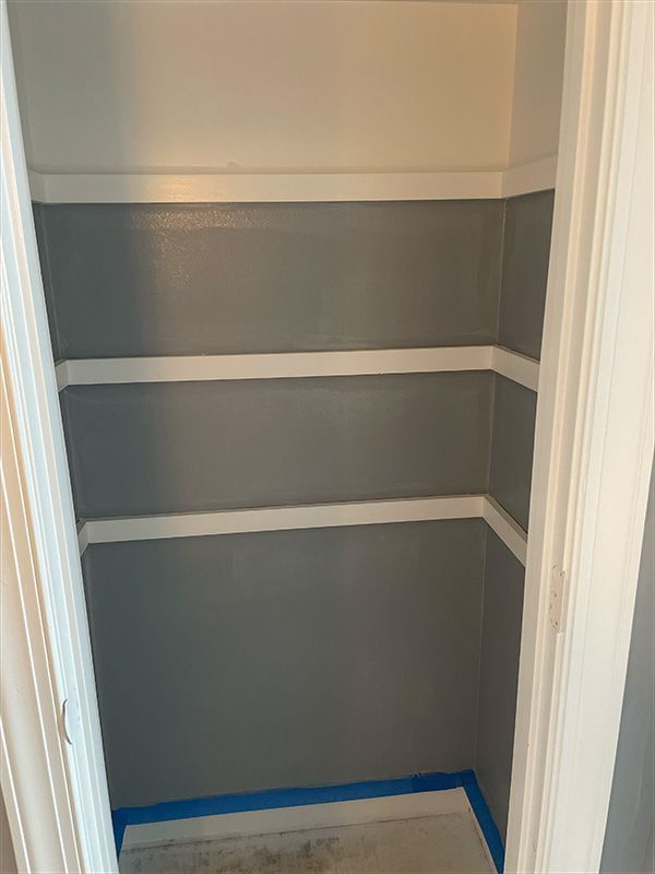 Empty closet interior with three shelves, painted gray and white, blue tape on floor.