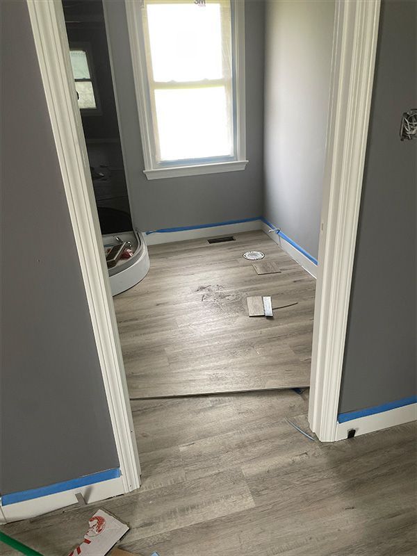 Bathroom with gray walls and light wood-look flooring being installed. Window visible.