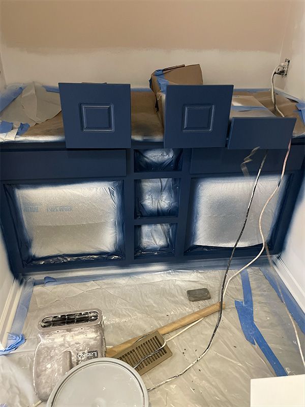 Blue painted bathroom cabinet, doors and drawers, with painter's tape and plastic sheeting. 