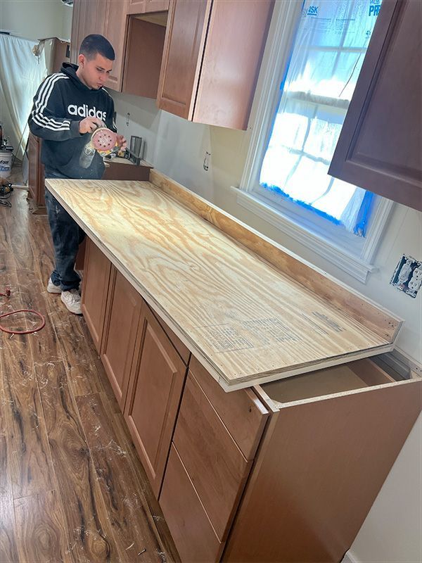 Man installing a countertop in a kitchen. Cabinets and a window are visible.