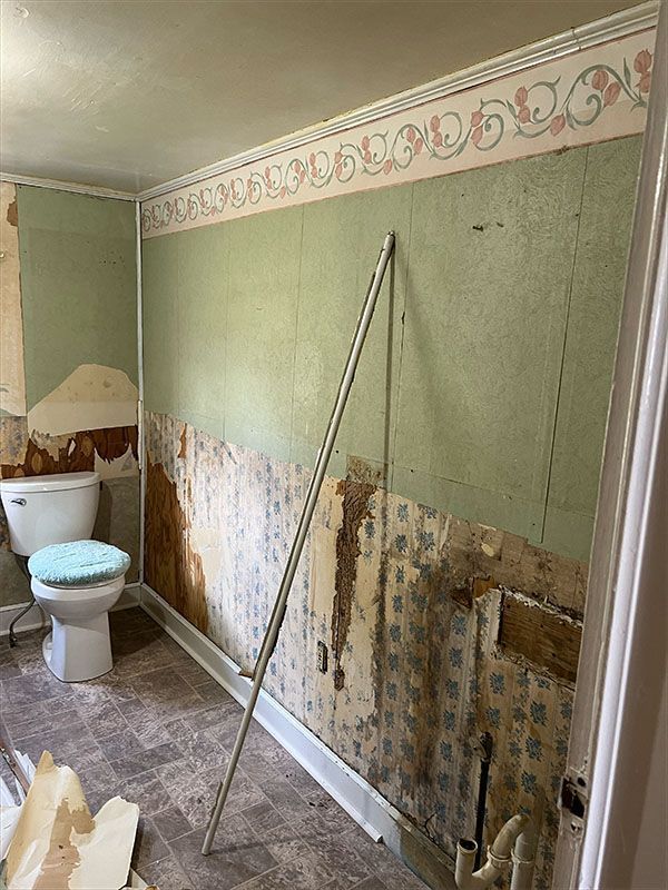 Bathroom with partially stripped green walls, toilet, and a support pole.