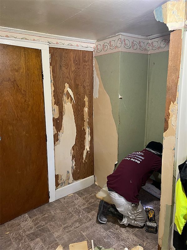 Person removing wallpaper in a room with a closed wooden door. Walls are partially stripped.