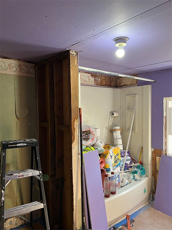 Bathroom renovation, studs exposed. Tub, supplies, ladder. Purple walls, ceiling, and drywall.