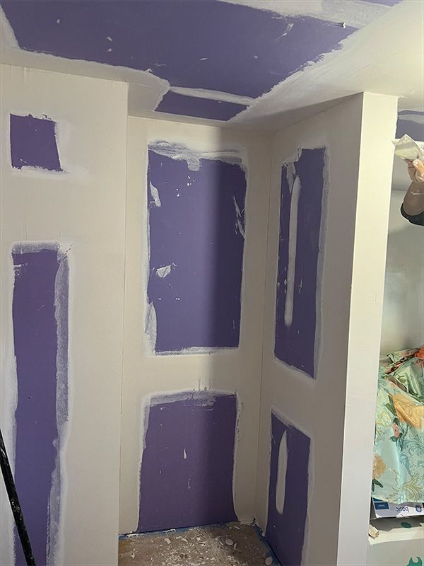 Interior corner with purple drywall patches and white walls. Room appears under construction.