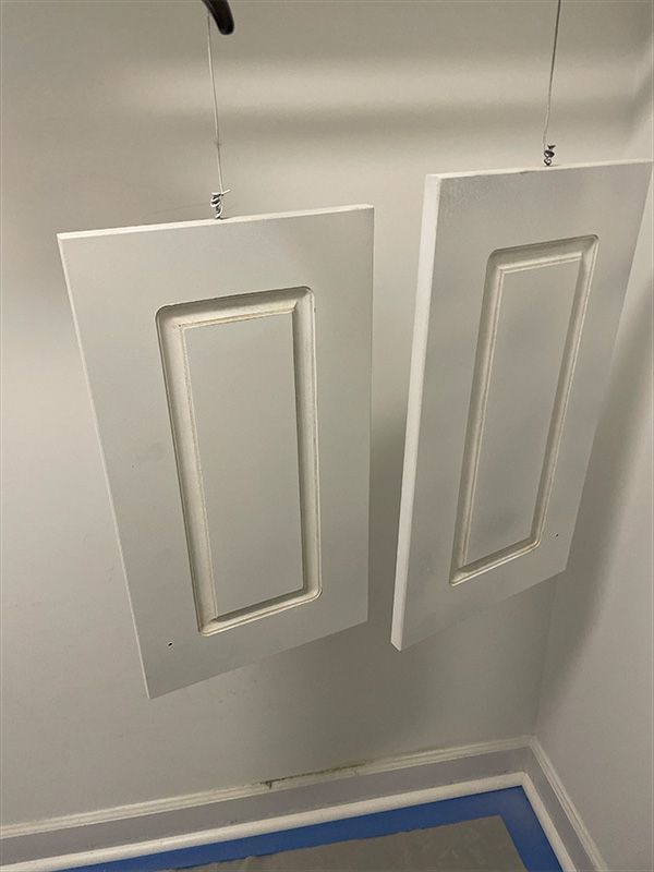 Two white painted cabinet doors hanging on wires, drying in a corner.
