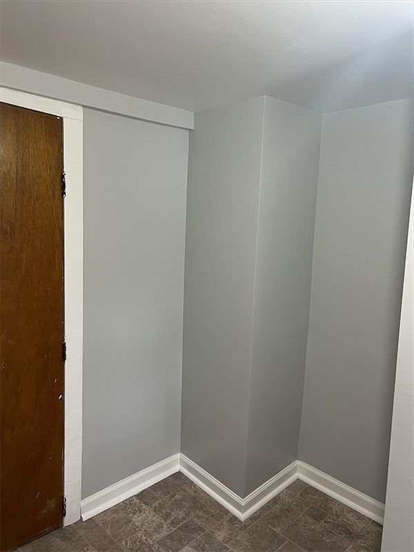Corner of room with gray walls, white trim, and a dark wooden door on the left.