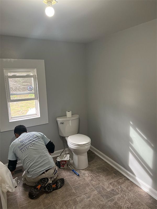 Person painting bathroom walls gray; toilet and window visible.