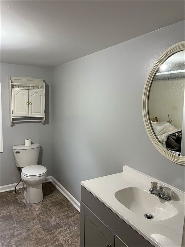 Bathroom with gray walls, toilet, vanity, and a round mirror.
