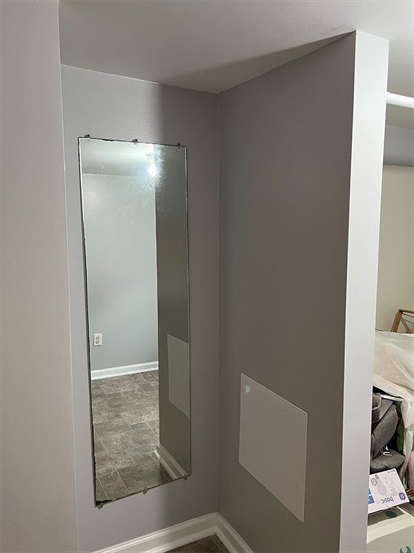 A long, rectangular mirror in a gray corner. The floor has a brown tiled pattern.