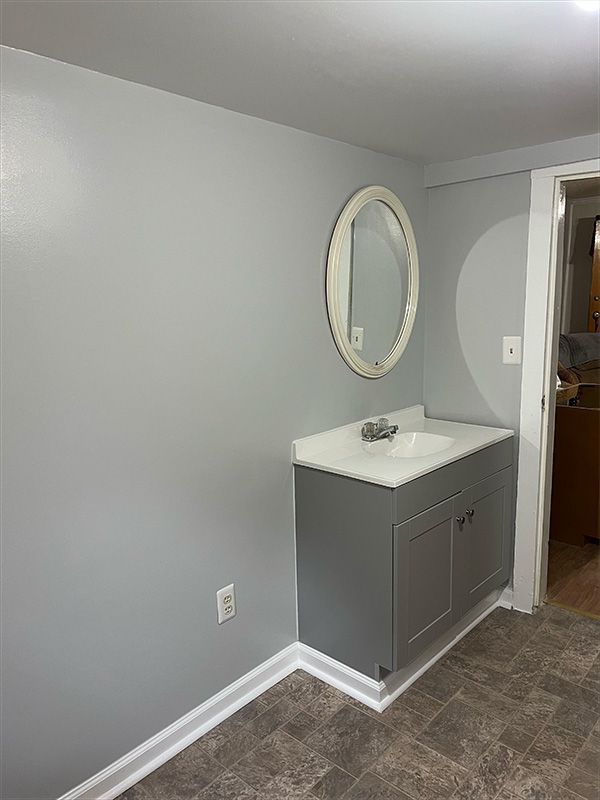 Gray bathroom vanity with oval mirror, white countertop, and light gray walls.